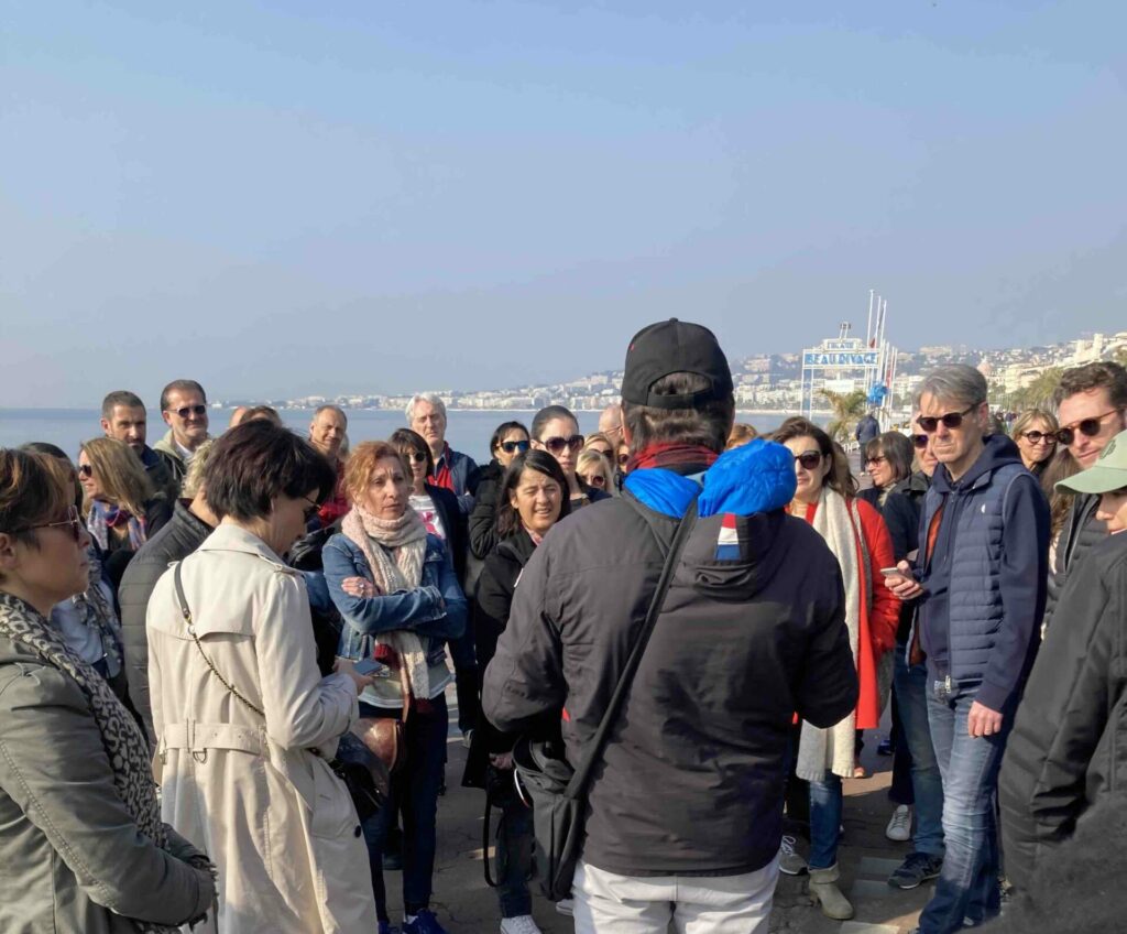 Un groupe de personnes lors du briefing de départ d'un jeu de Team Building à Nice, sur la promenade des anglais avec la Mer Méditerranée en arrière-pan de la photo.