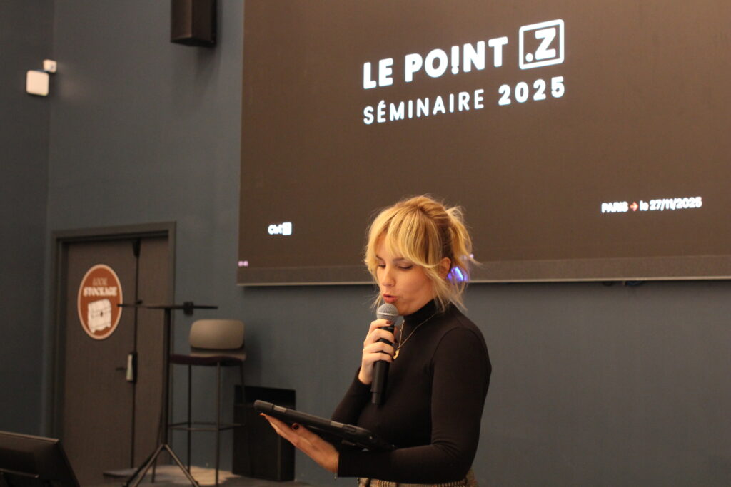 une animatrice au micro lors d'une présentation de convention entreprise. Derrière elle, un dispositif de couleur noir avec le nom de l'entreprise.