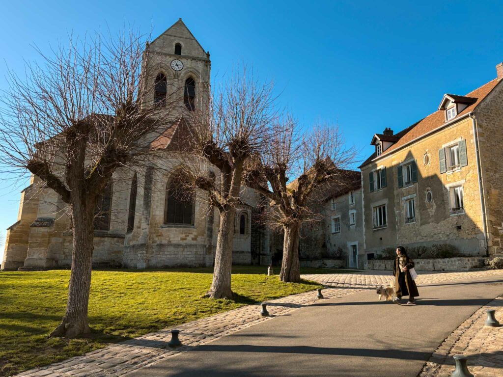 une route en pente avec derrière une église  et des maisons en pierres sous le ciel bleu.
