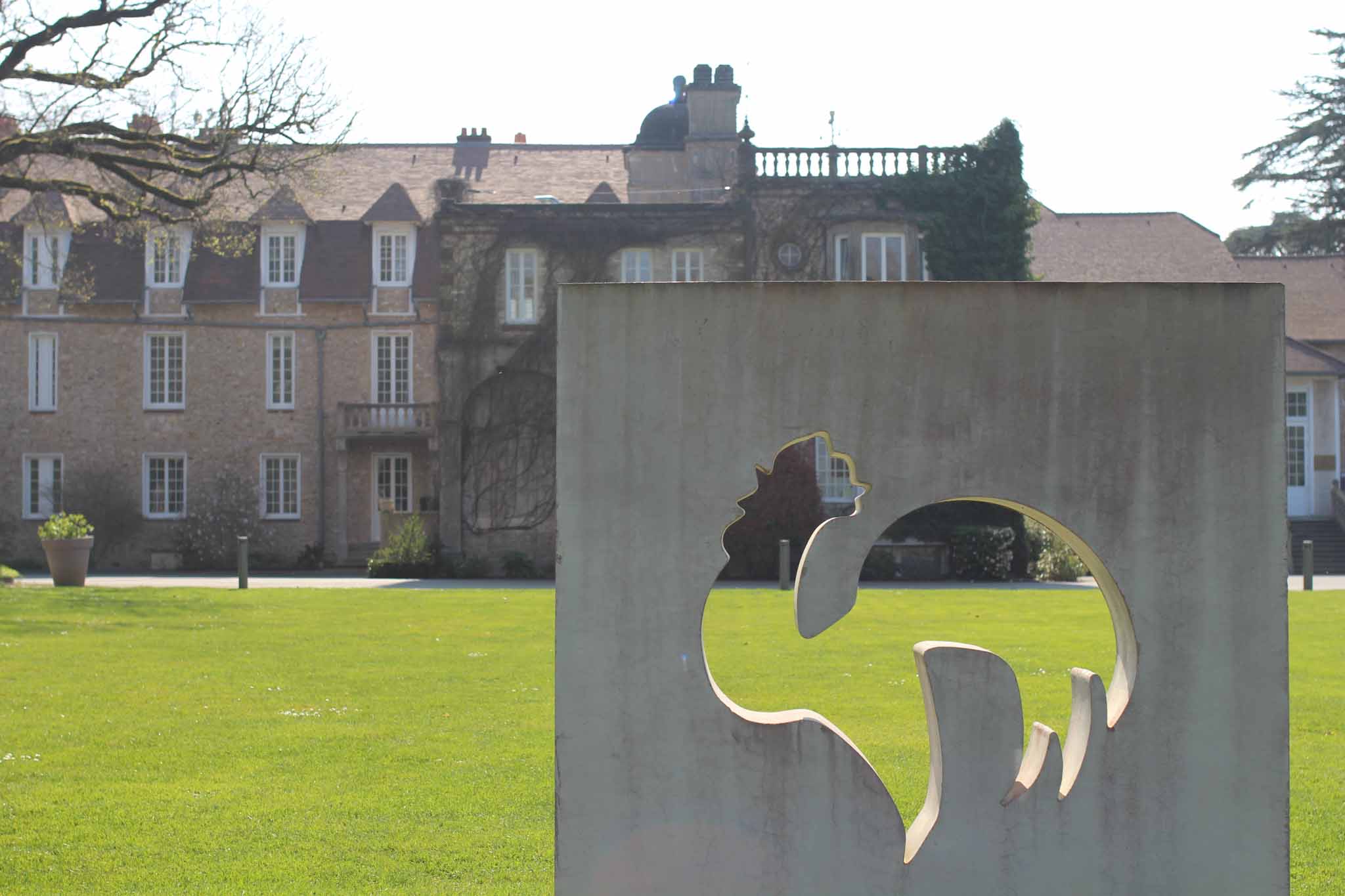une sculpture en pierre du Coq de l'équipe de France de Football dans un parc avec un chateau derrière
