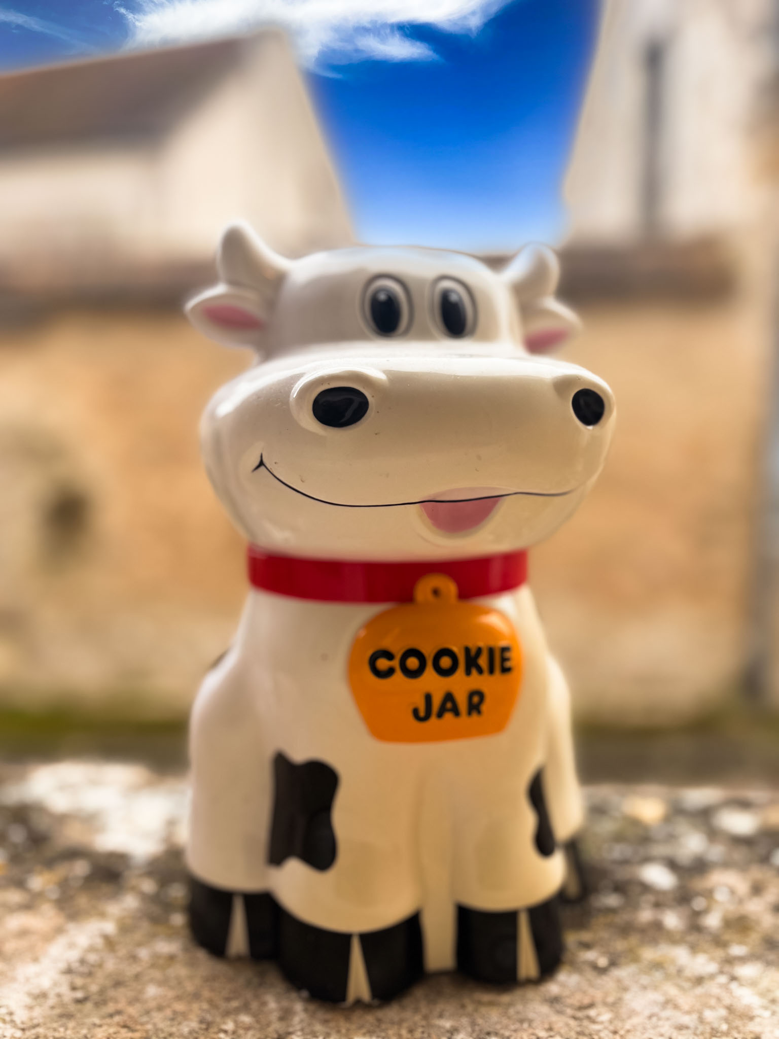 une tirelire en forme de vache avec en arrière plan un village avec des maisons en pierre