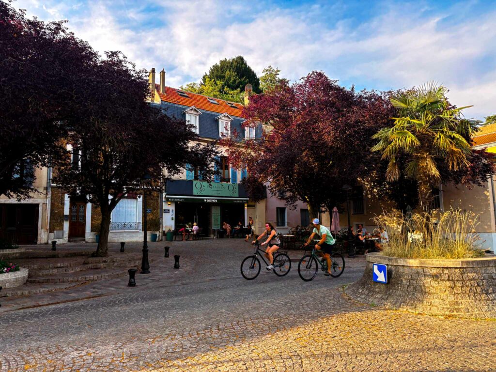 une place en pavés avec deux vélos, un palmier et un restaurant en arrière plan