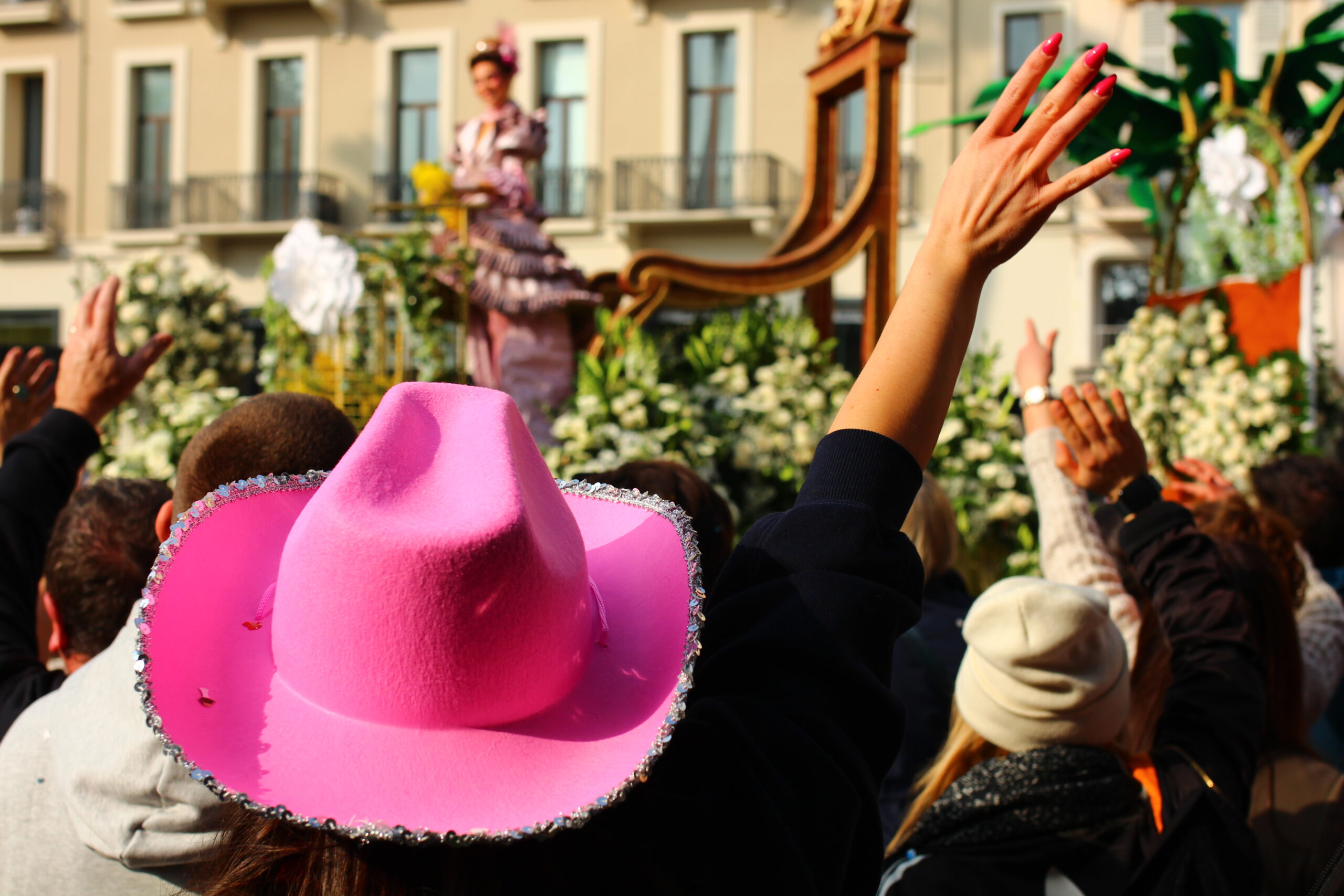 Femme de dos avec un chapeau style cowboy couleur rose qui lève le bras lors d'une fête populaire