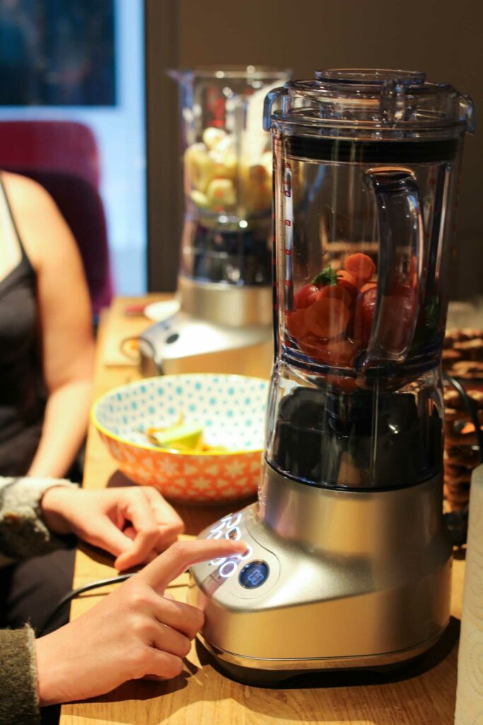 deux blenders avec des fruits et légumes et une main qui actionne le bouton on d'un des deux blenders.