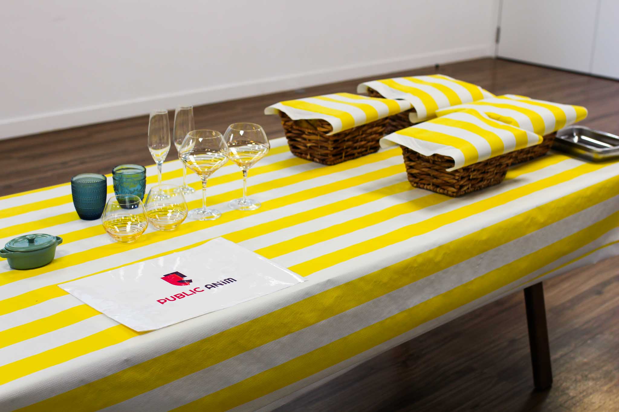 table avec une nappe jaune et blanche et dessus des verres de différentes tailles et 4 paniers.